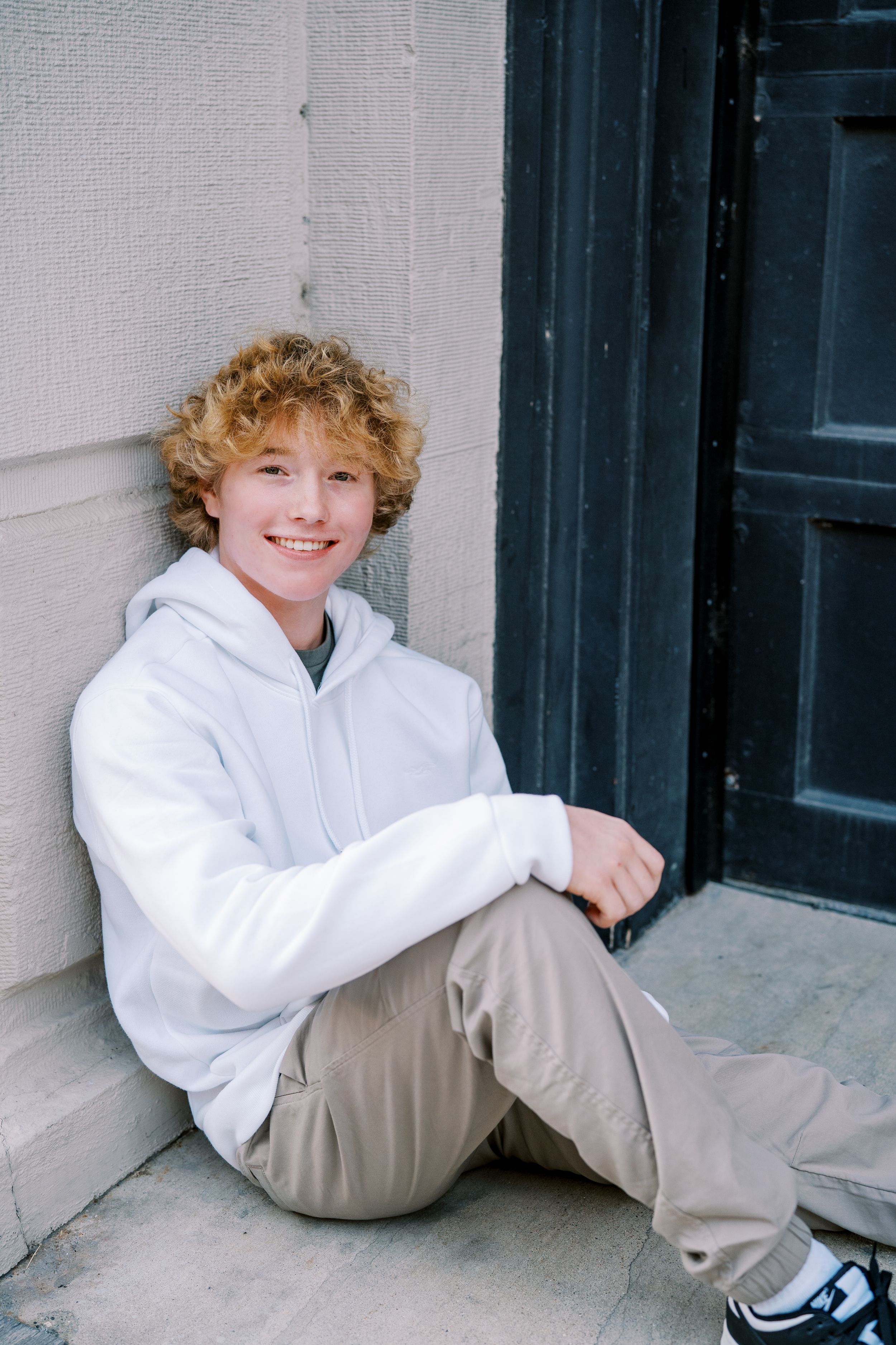 Casual poses against white wall and dark door wearing white hoodie.