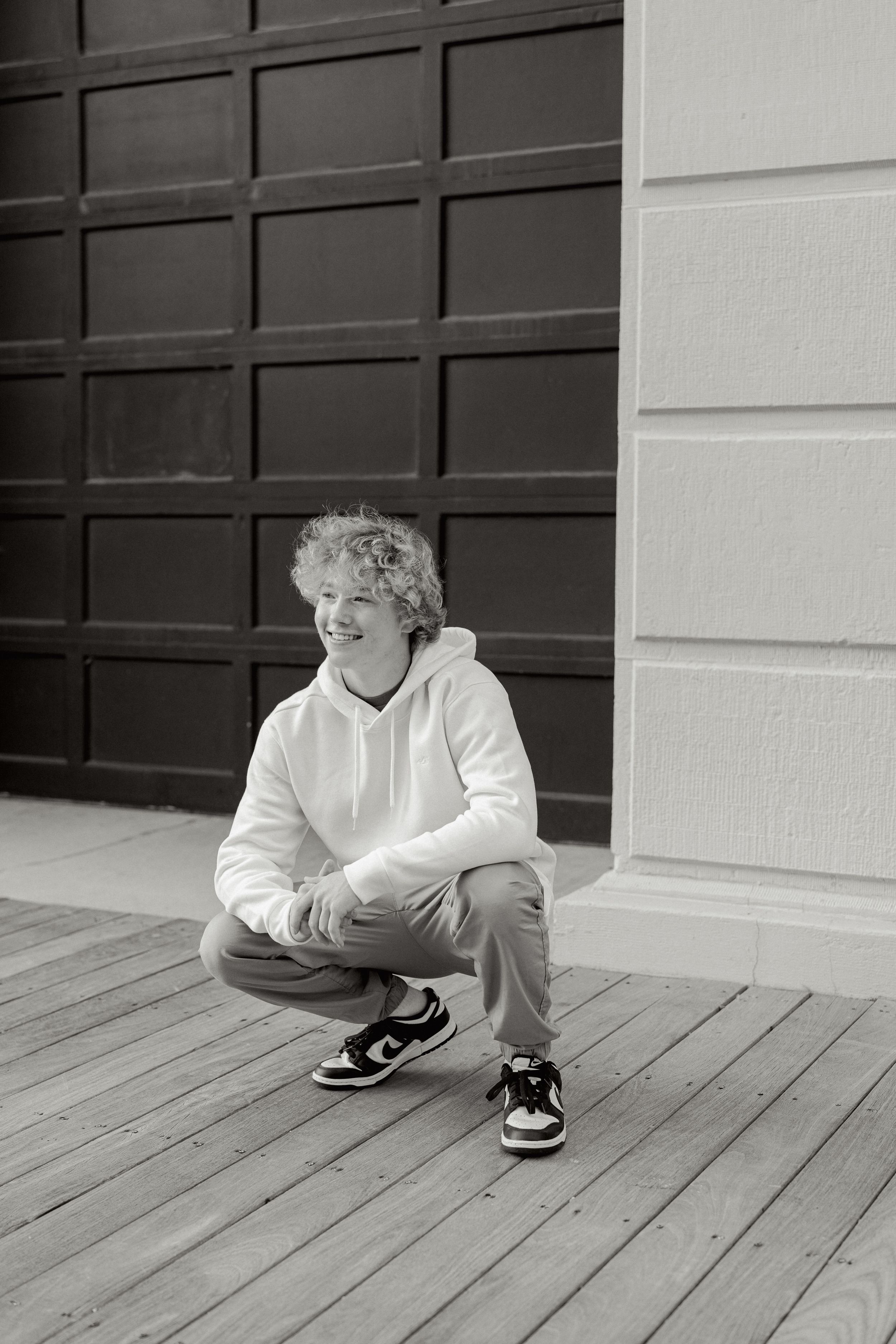 Black and white portrait series on wooden deck wearing white hoodie.