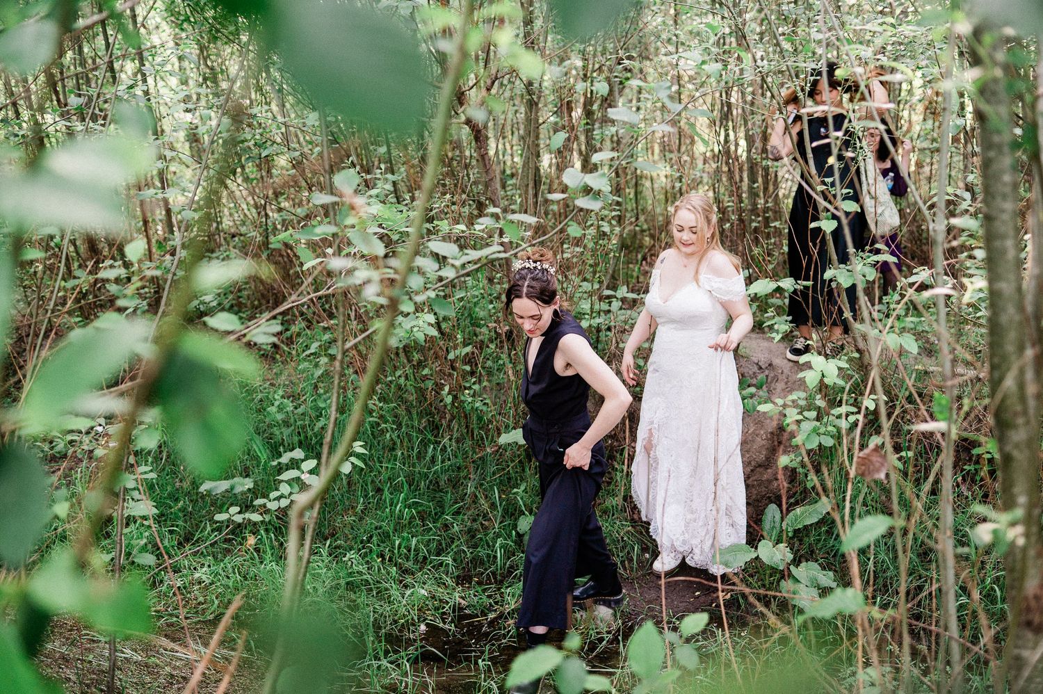 a couple crosses through a stream in a heavily forested setting