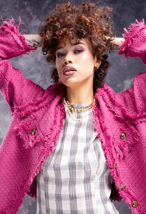 Girl in a plaid dress and blazer, hands in her hair, looking down to the camera