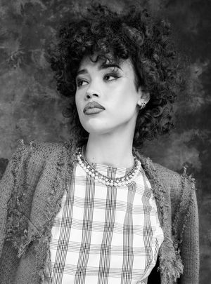 Black and white photo of a girl in a plaid dress, a blazer, looking left