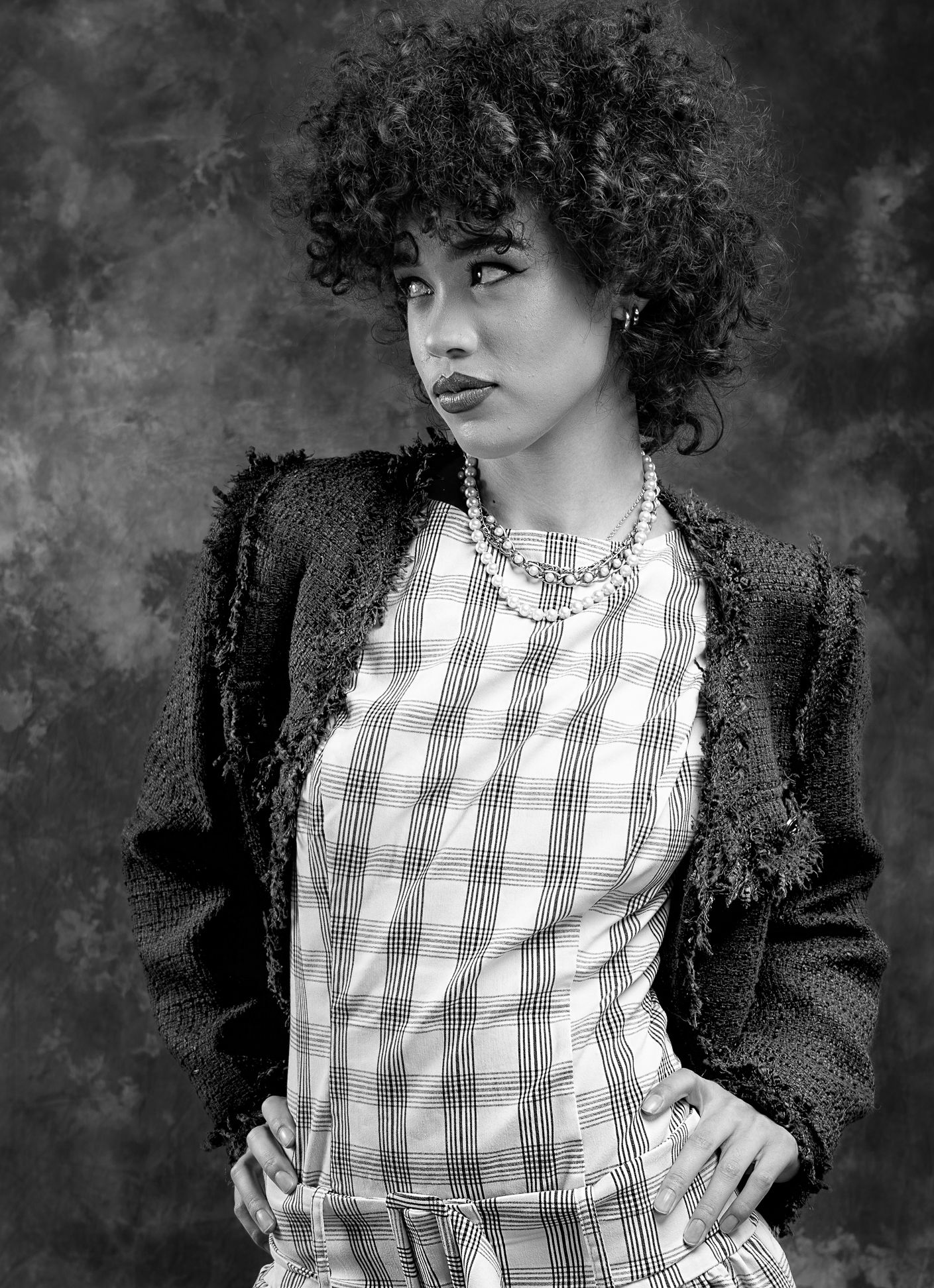 Girl in a plaid dress and blazer, hands on hips, looking left
