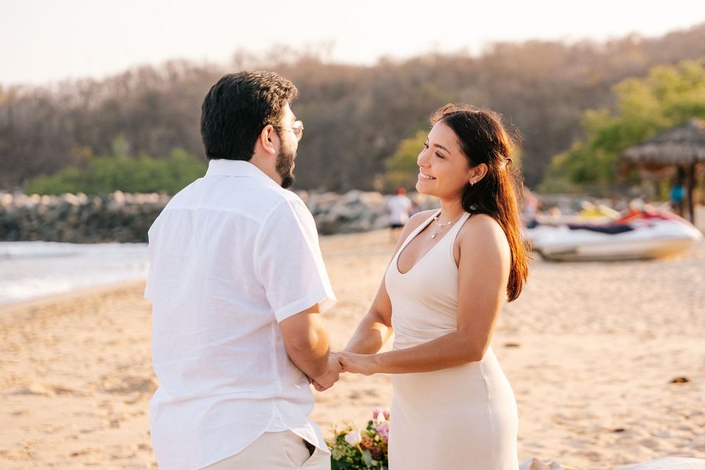 A couple dances together on a sandy beach at sunset during a romantic photoshoot.