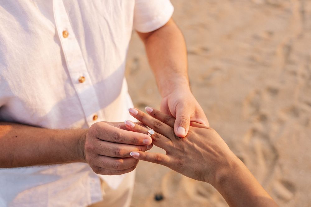Close-up shots of hands exchanging wedding rings during an outdoor beach ceremony.