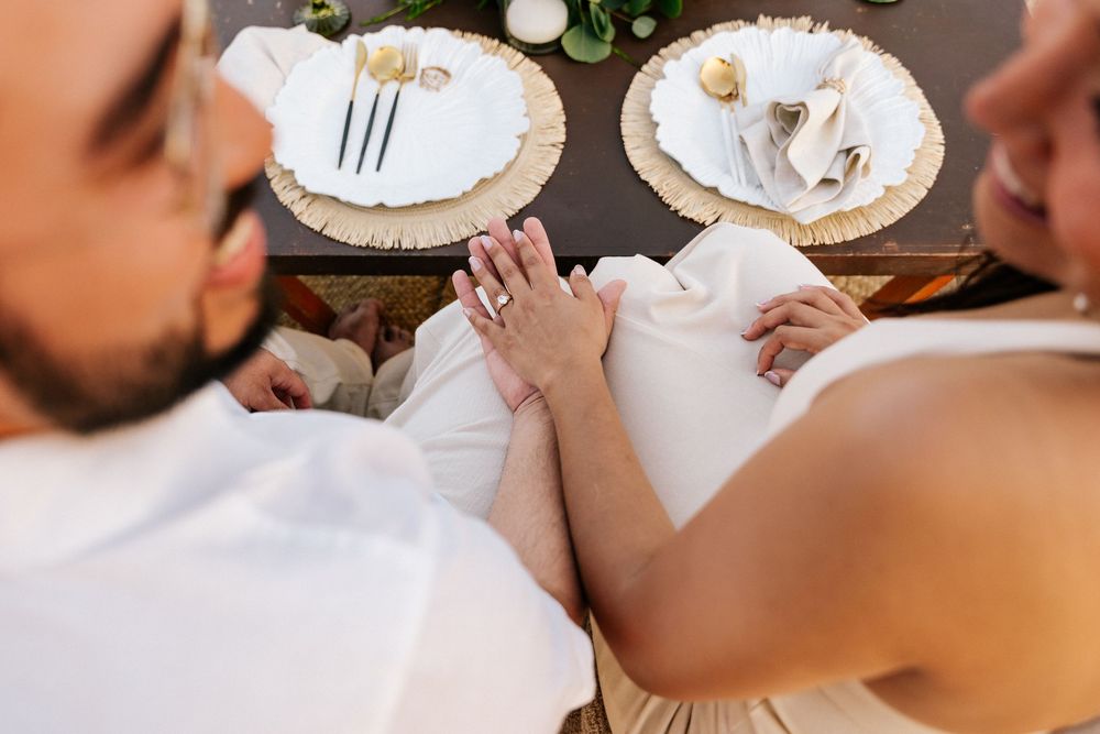 A couple holds hands while sitting at an elegant table setting with white plates and floral decorations.