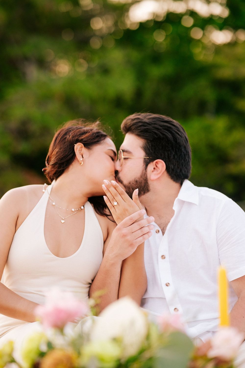 A romantic couple in white attire sharing tender kisses outdoors with soft bokeh lighting in the background.