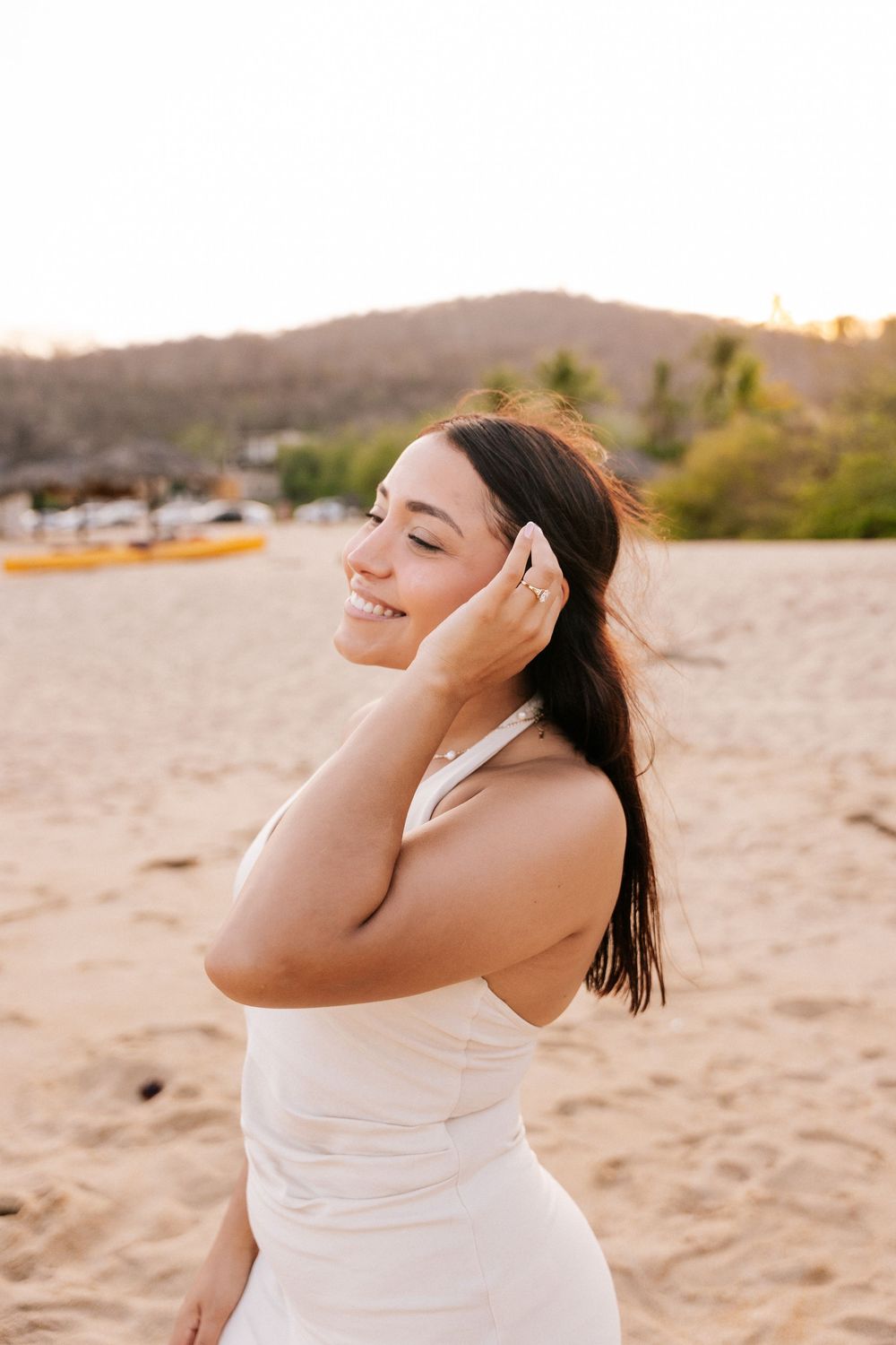 Person in white top enjoying music with headphones on sandy beach at sunset.