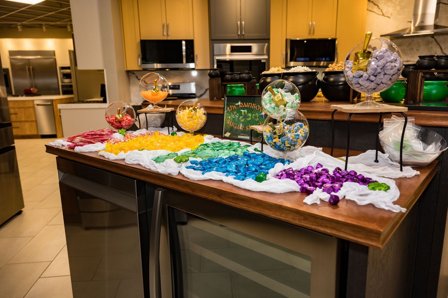 Rainbow-colored candy buffet display arranged in rows across a wooden kitchen island counter.