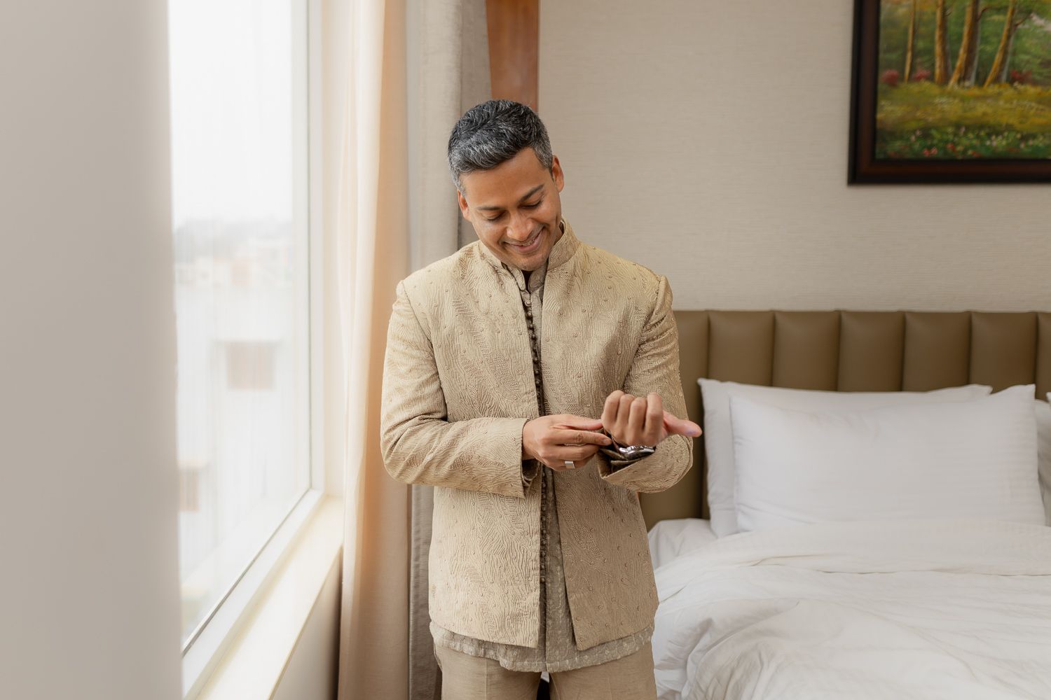 A person in a beige suit looks at their phone while standing in a bright, modern interior space.