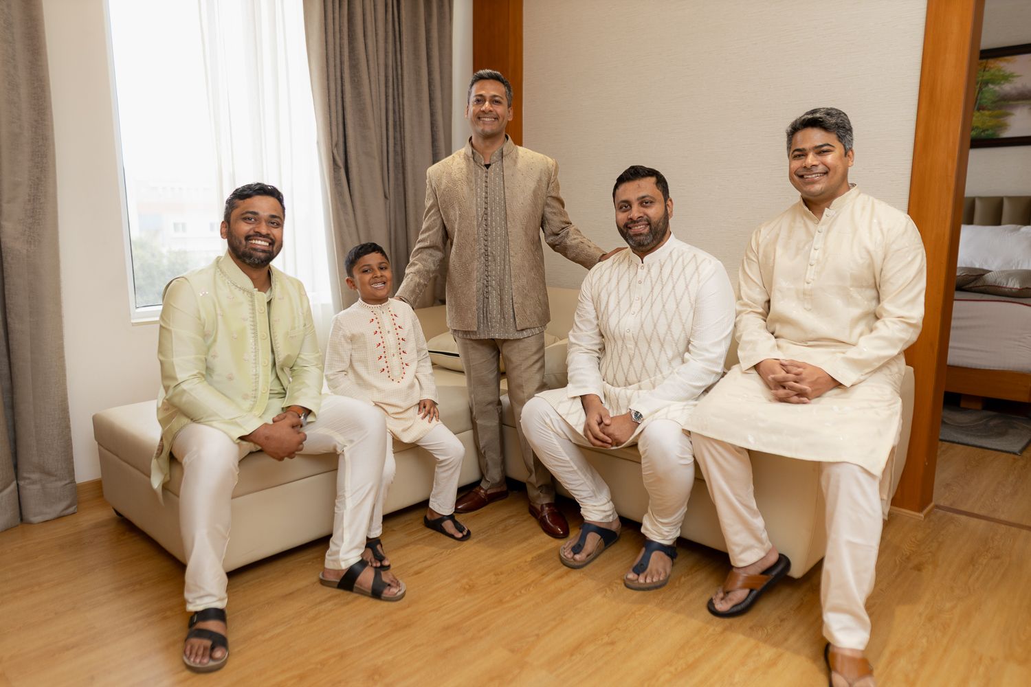 A group of people wearing all white outfits sit together on the floor in what appears to be a living room setting.