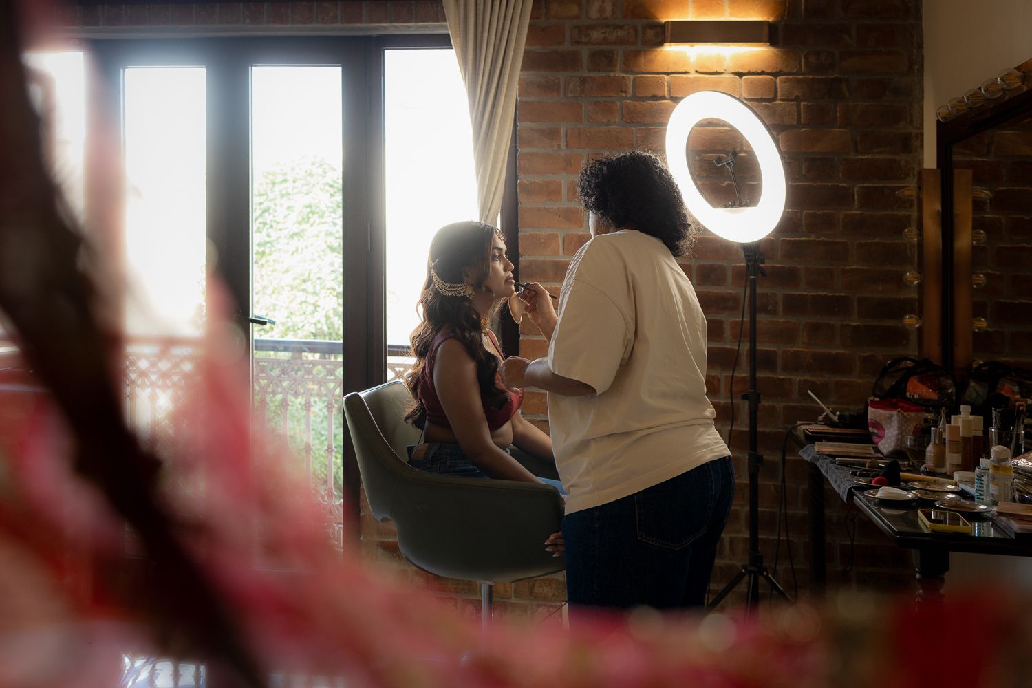 Behind the scenes at a photo shoot in a brick-walled studio with ring light and window lighting.