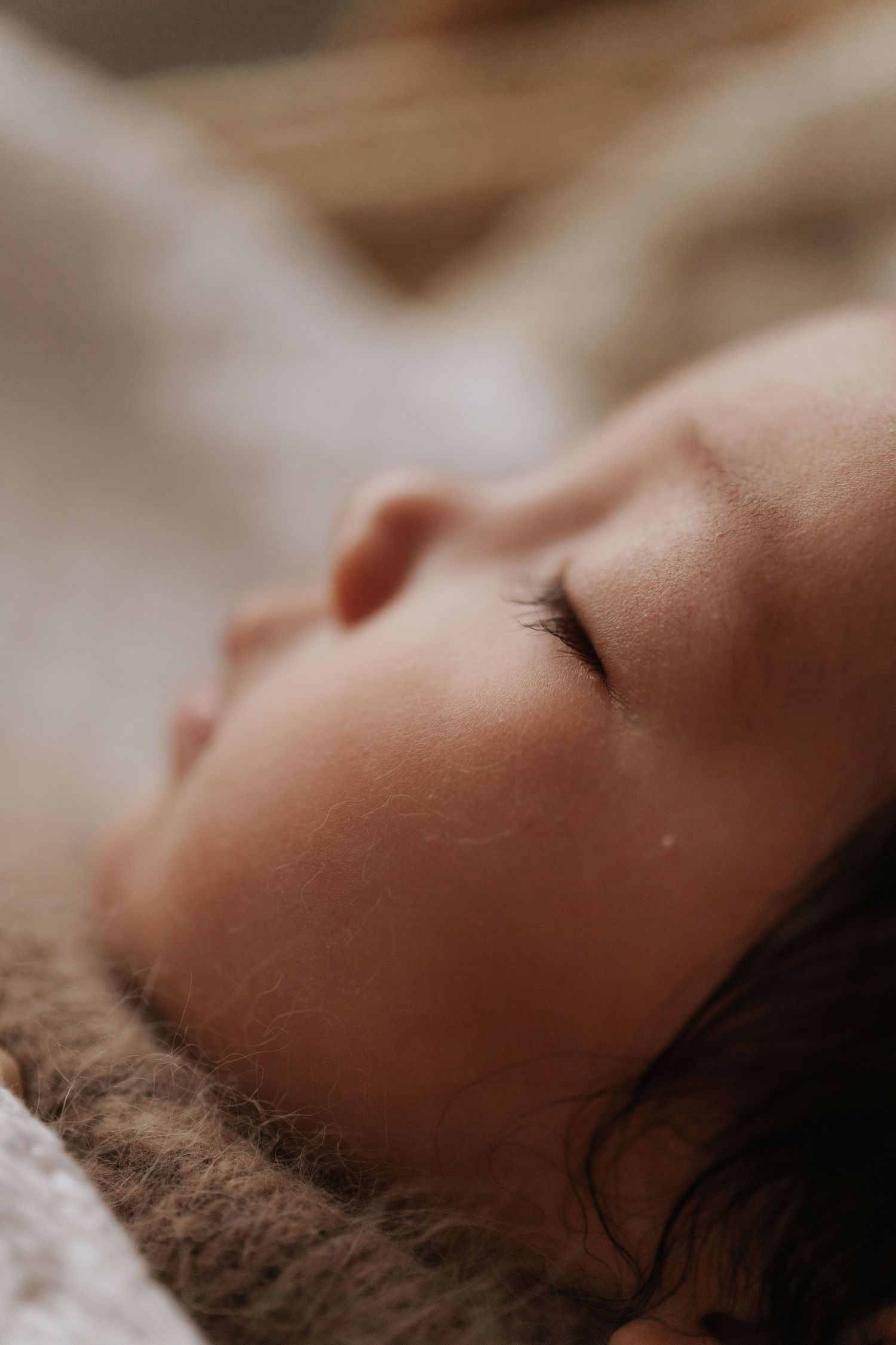 Close-up of a peaceful sleeping newborn baby with delicate eyelashes, resting on a soft brown blanket.