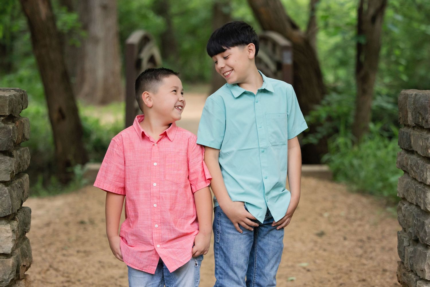 Two young boys in button-down shirts stand together and share a laugh on a wooded trail in Colleyville, TX.