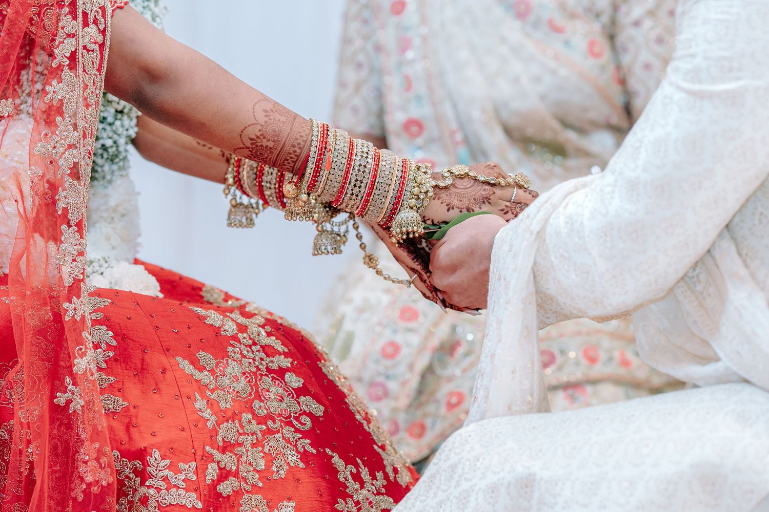 Indian bride and groom exchanging hands during traditional wedding ceremony, bride wearing red lehenga with gold bangles.