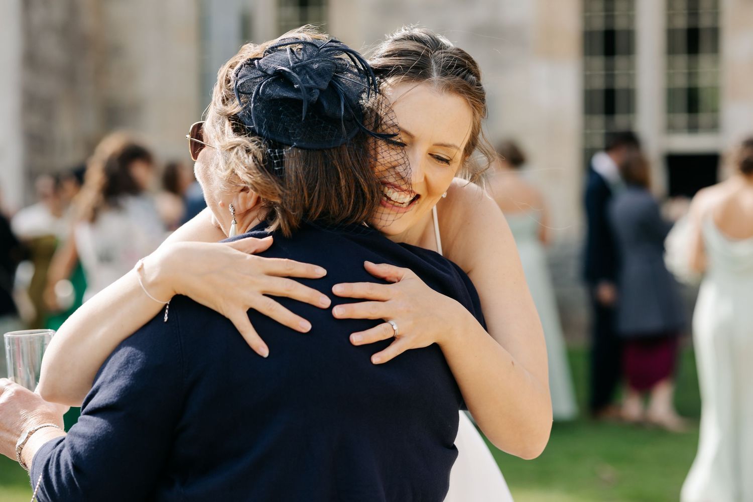 Joyful wedding guests share warm embraces and hugs during an outdoor celebration at a historic venue.