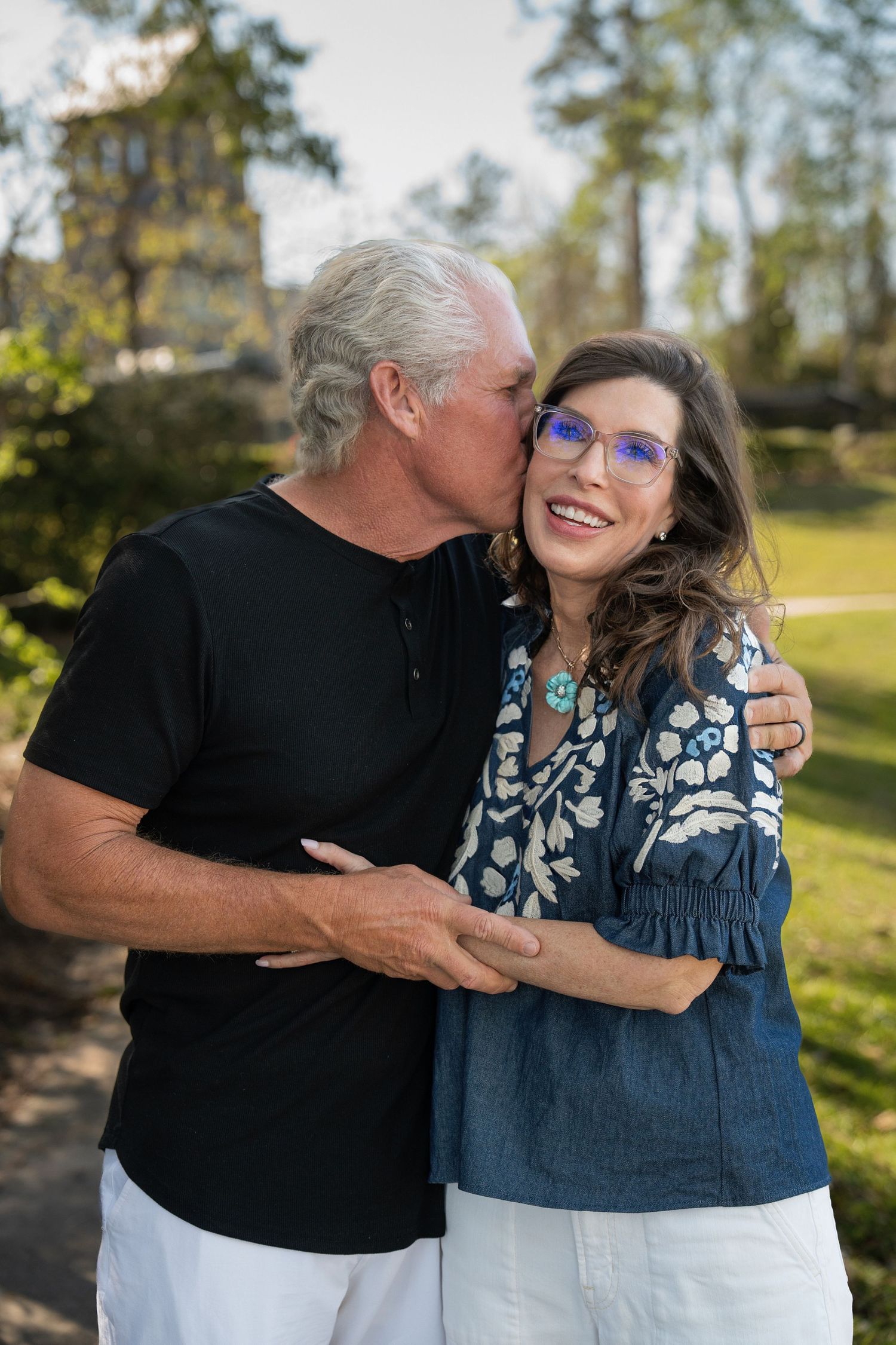 A couple embraces and shares affectionate moments in a sunny outdoor setting with trees in the background.