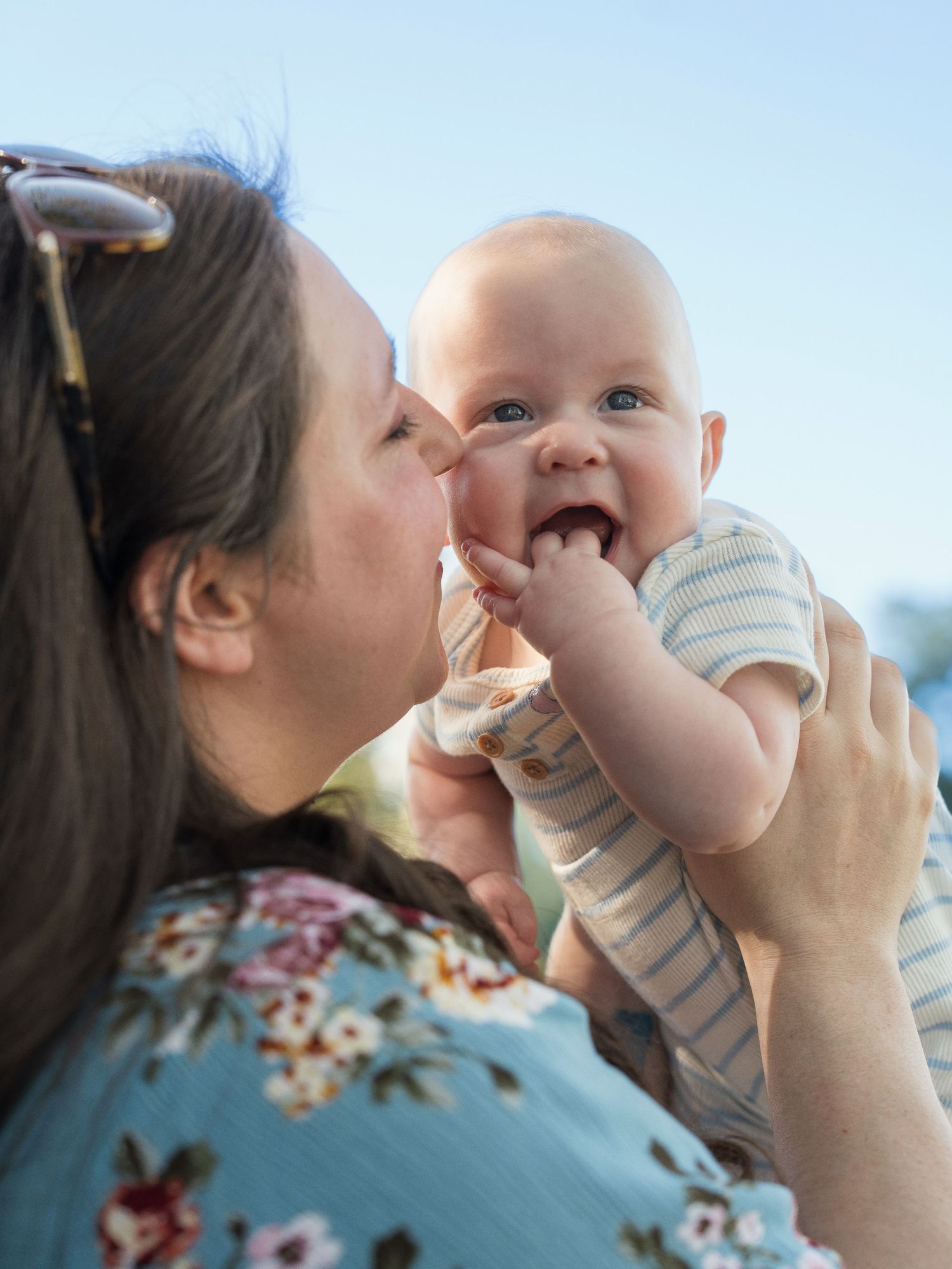 A tender moment between parent and baby as they share playful interactions against a bright blue sky background.