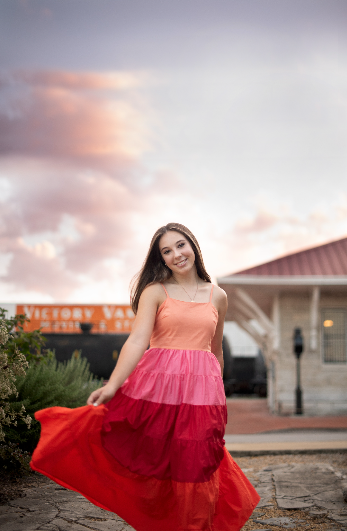 A flowing red and pink ombre dress twirls gracefully against a sunset sky in a creative outdoor photoshoot.