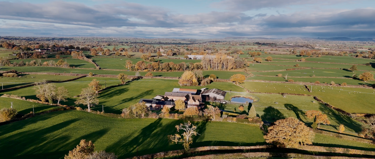 Aerial panoramic view of rolling countryside with patchwork fields and scattered buildings.