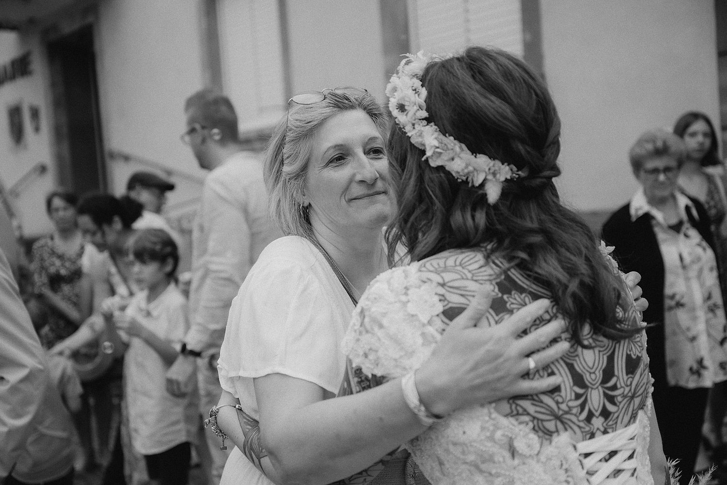 Emotional mother hugging bride in floral crown at outdoor wedding ceremony in black and white.