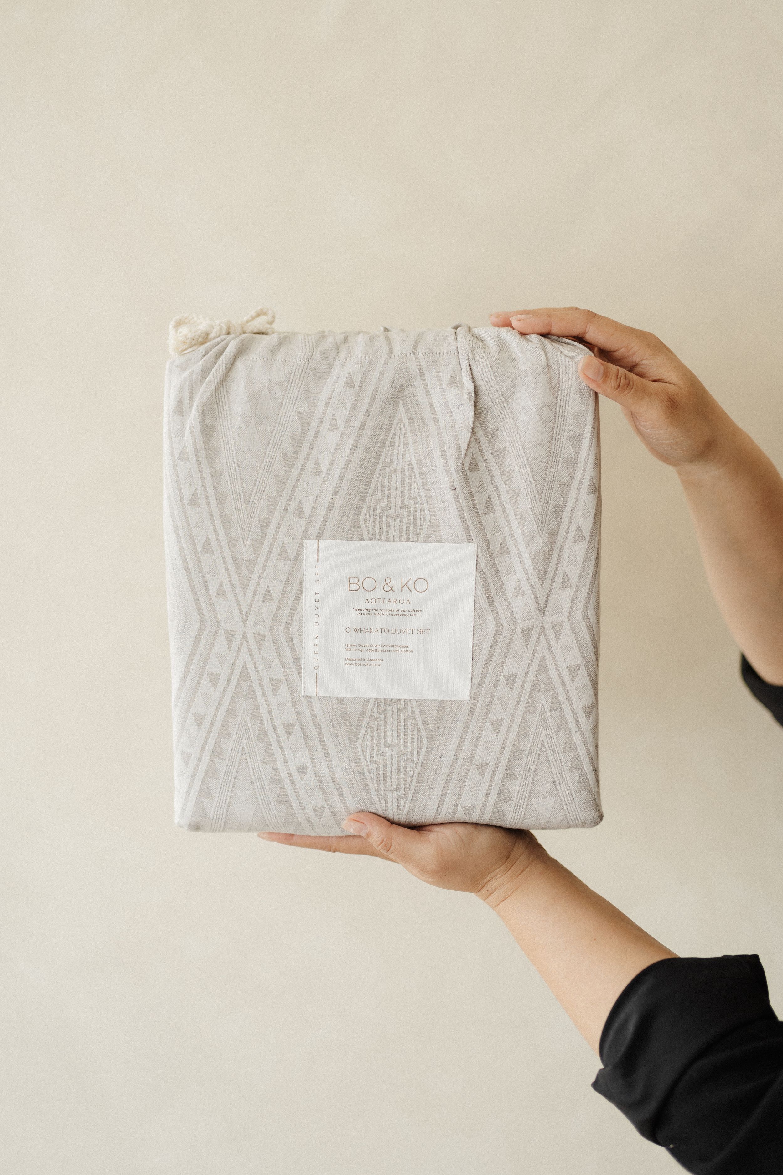 Hands holding a folded gray textured fabric with a white label against a neutral background.