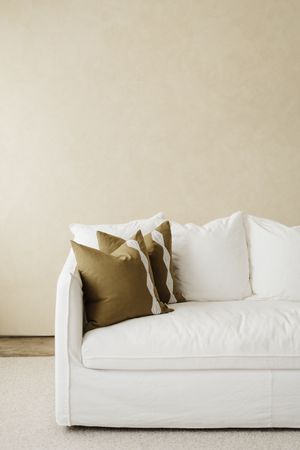 White modern sofa with beige throw pillows against neutral wall in minimalist living room setting.