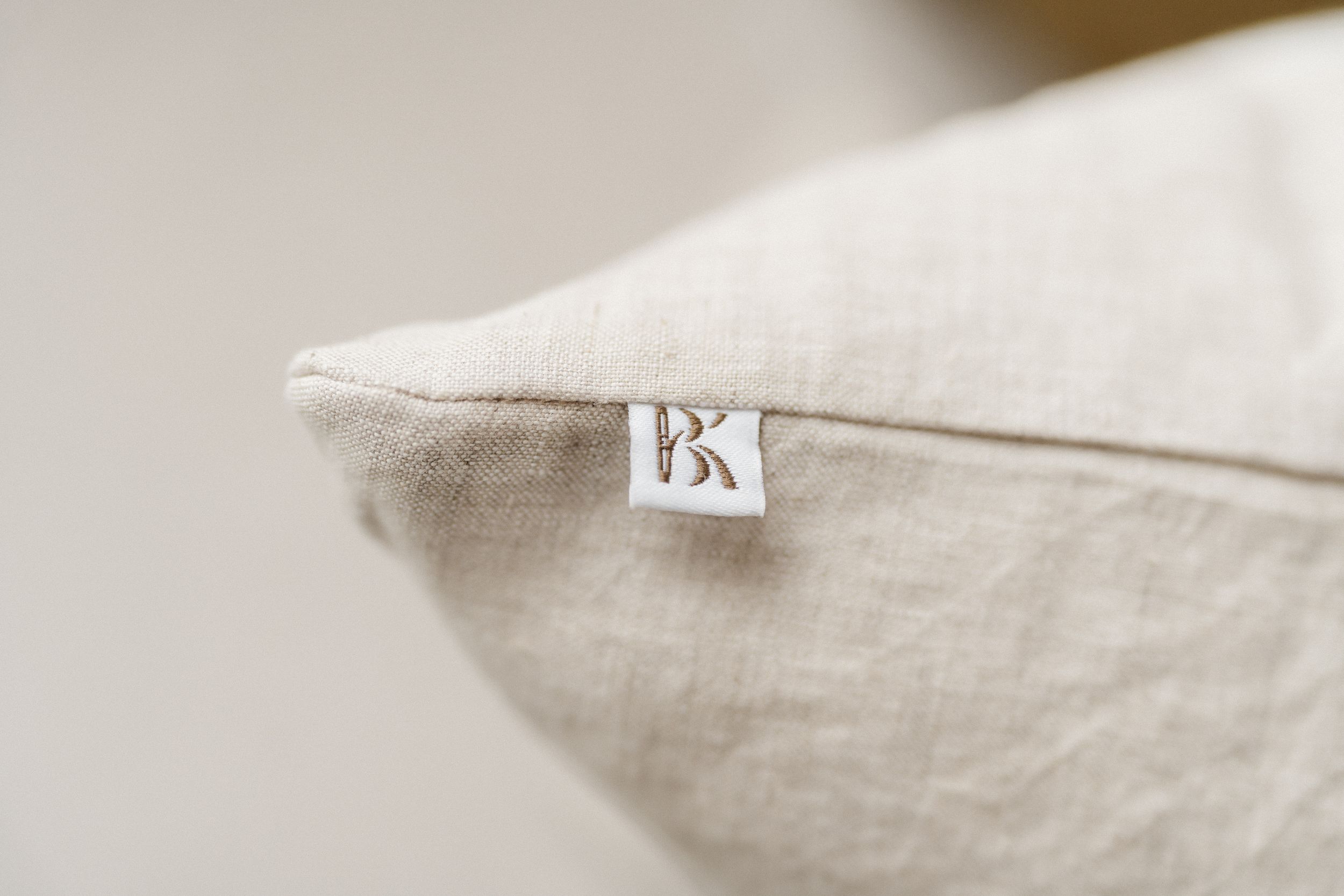Close-up view of a white linen pillow with a small BK label tag sewn into the seam.