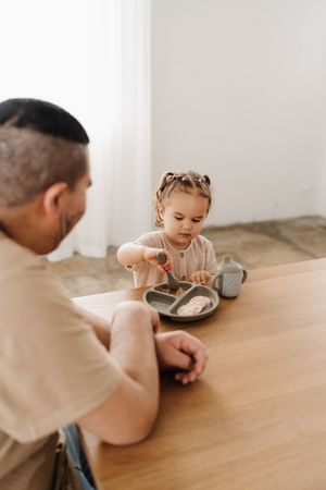 Child sitting at wooden table during mealtime in minimalist white room.
