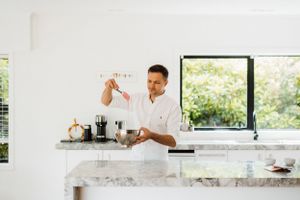 Bright modern kitchen interior with person preparing ingredients at marble countertop.