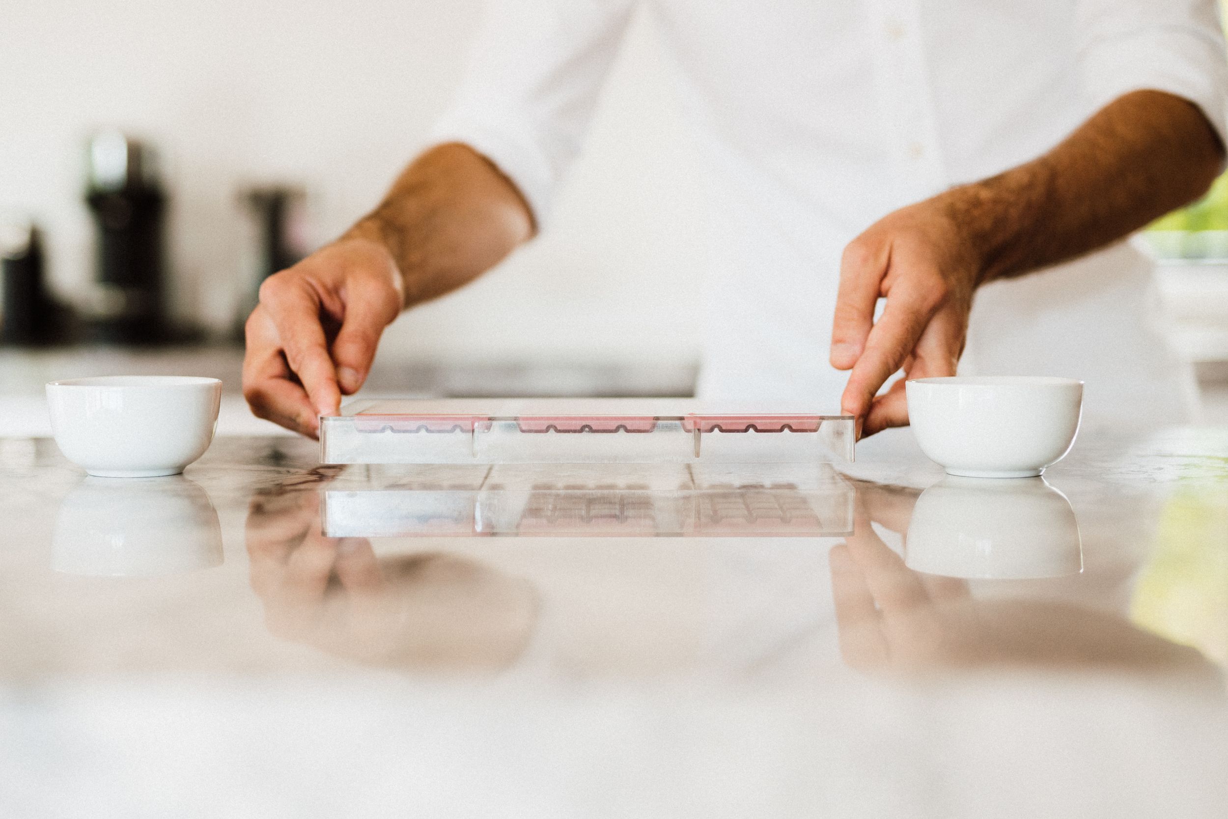 Minimalist white kitchen counter workspace with hands working on ingredients.