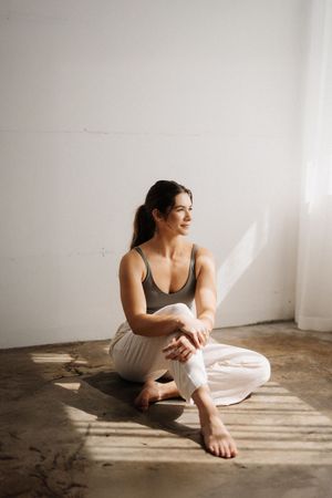 A figure sits on a wooden floor in casual loungewear, creating a minimalist portrait series in natural light.