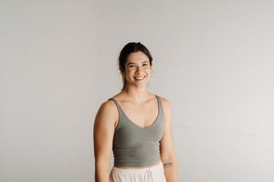 Woman in gray workout top smiles while posing against white background.