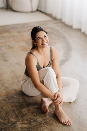 A casual lifestyle portrait shows someone sitting comfortably on the floor in neutral-colored clothing.