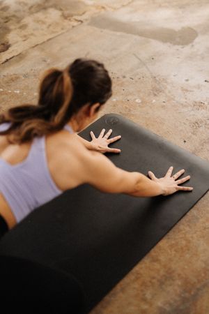 A sequence showing a person in a purple tank top rolling out a black yoga mat on a concrete floor.