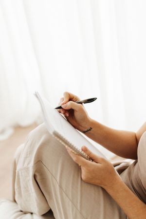 Close-up of hands writing in notebook against light background.