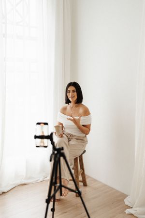 Person poses on stool for camera setup in bright minimalist studio.
