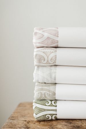 Stack of white folded linens with embroidered borders on rustic wooden surface.