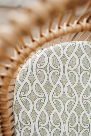 Close-up of rattan furniture edge with decorative swirled pattern fabric.