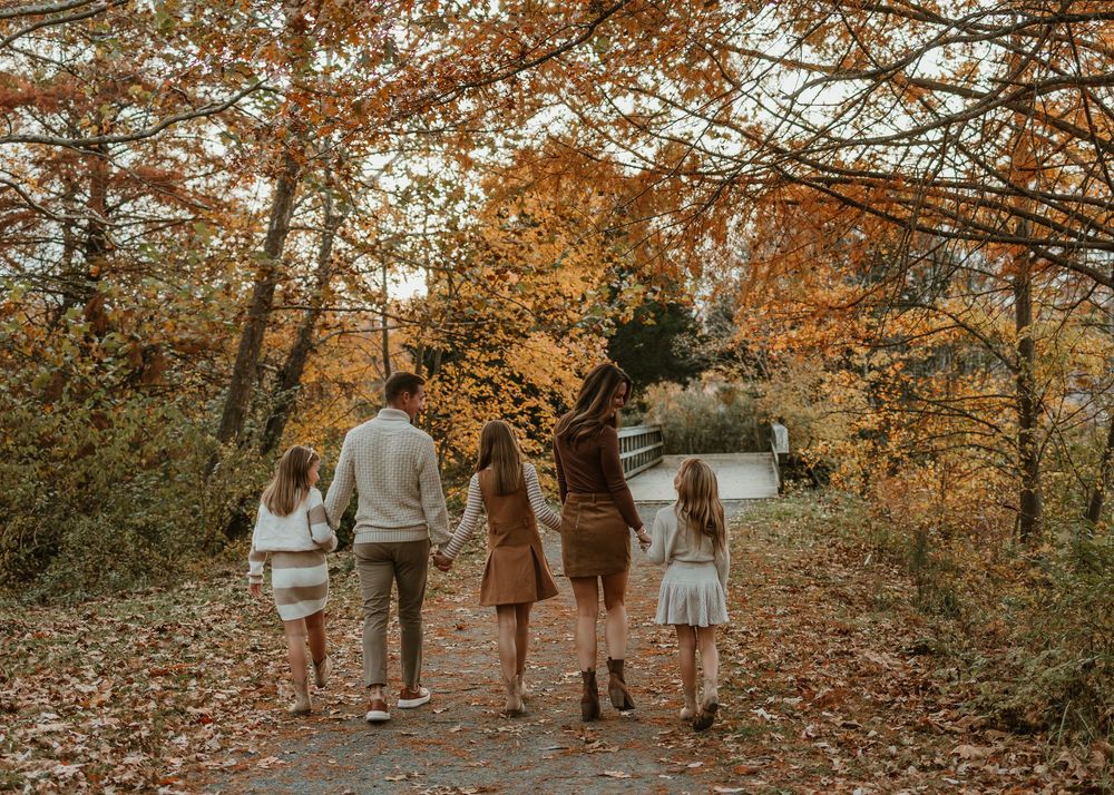 A group of people walk along a wooded trail in autumn with fallen leaves and golden foliage overhead.