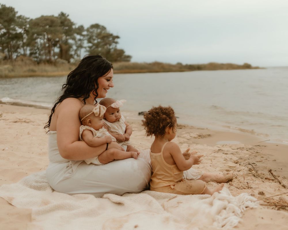 A family sits together on a peaceful beach at sunset with trees in the background.