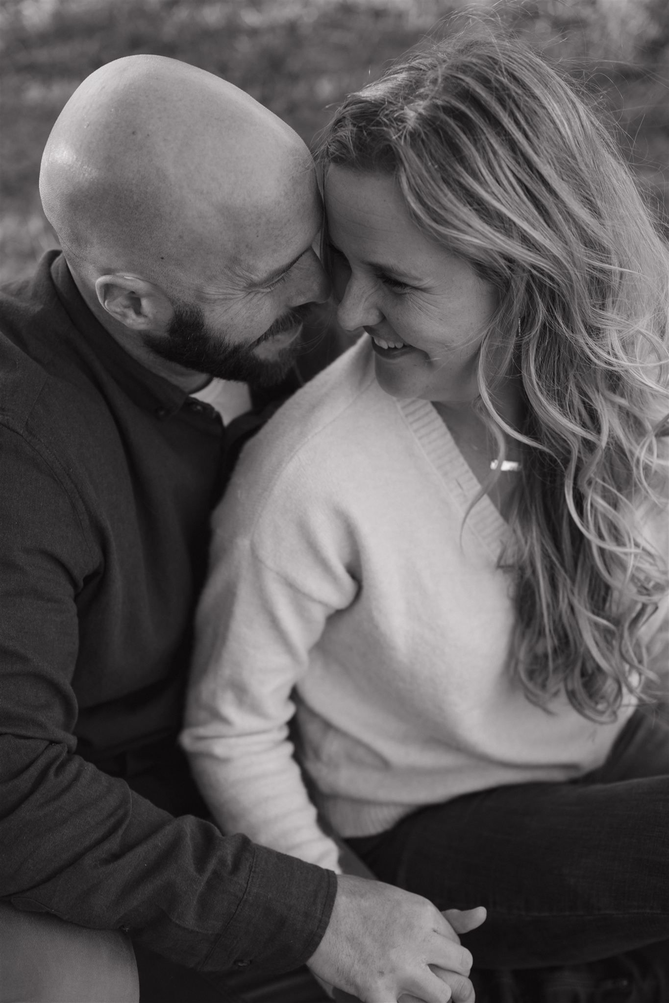 Black and white photo of a smiling couple embracing closely, bald bearded man and long-haired woman sharing a tender moment.