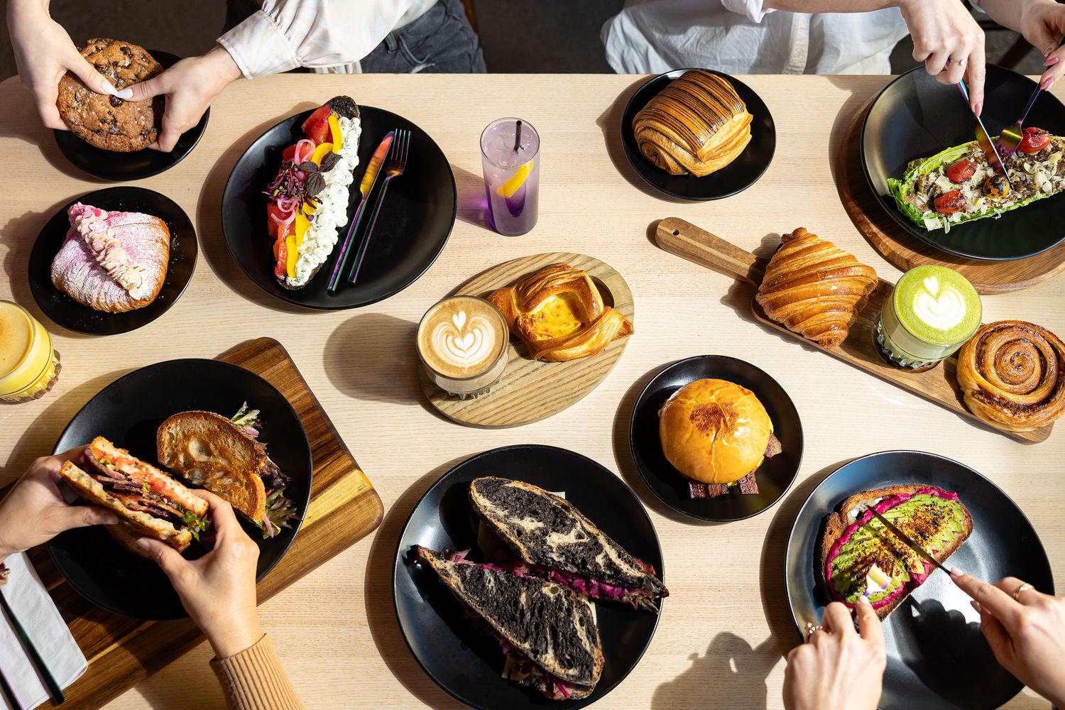 Overhead view of assorted gourmet food dishes on black plates at a modern cafe table.