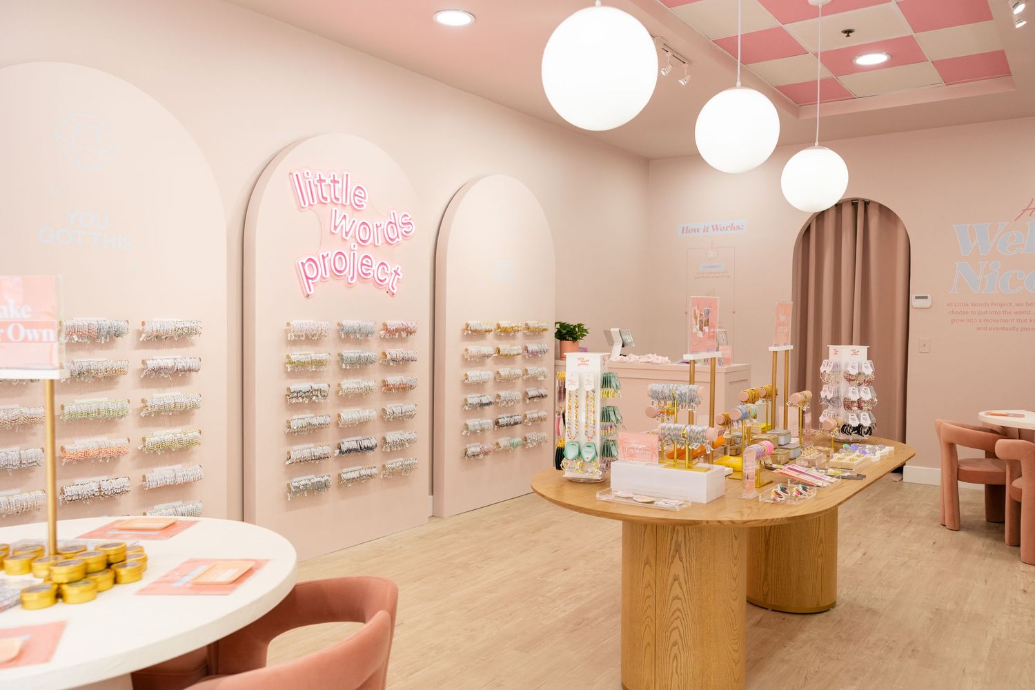 Bright pink retail store interior with arched displays, globe lights, and pastel decor.