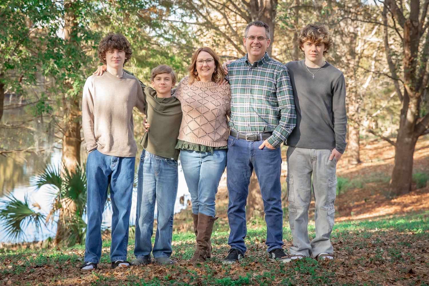 A group stands together in a casual outdoor setting among autumn trees and fallen leaves.