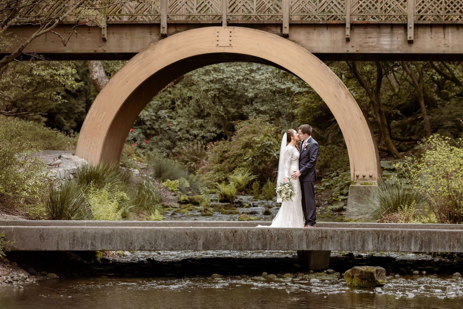 Black and white image of newlyweds walking away on wooden bridge.