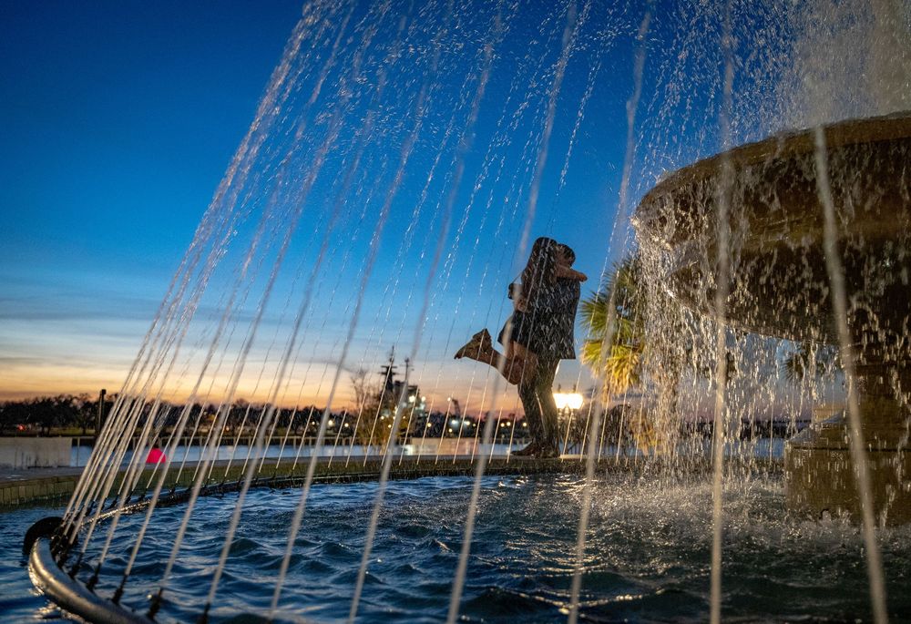 Water fountain sprays create a sparkling curtain effect against a vibrant blue sky and sunset background.