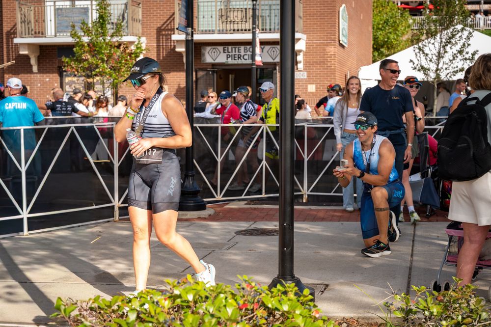 A runner in gray athletic wear passes by spectators at a race event along a city street with brick buildings in the background.