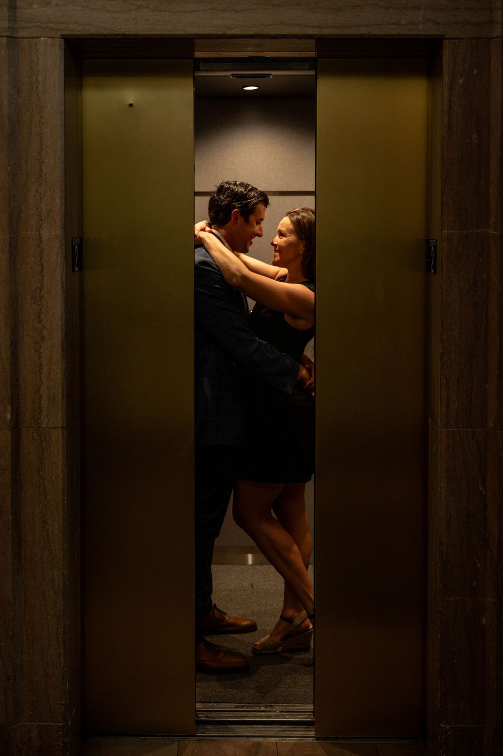 Silhouetted figures embrace in a dimly lit elevator doorway.