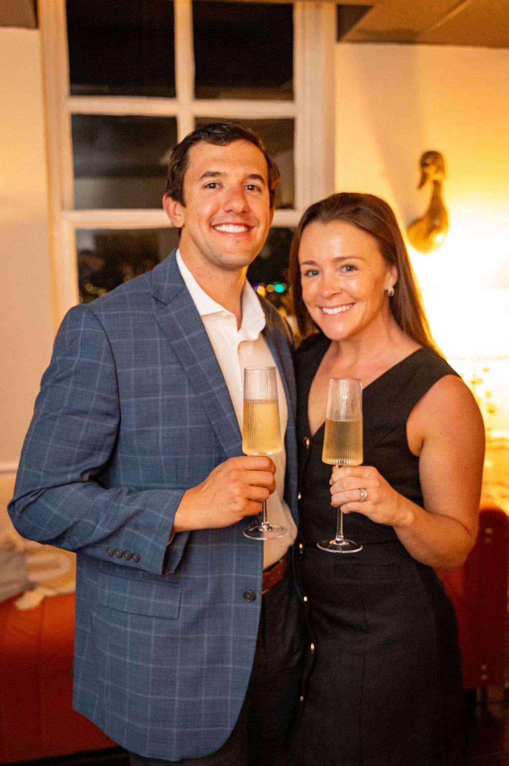 Couple in formal attire share champagne toasts at an elegant indoor celebration.