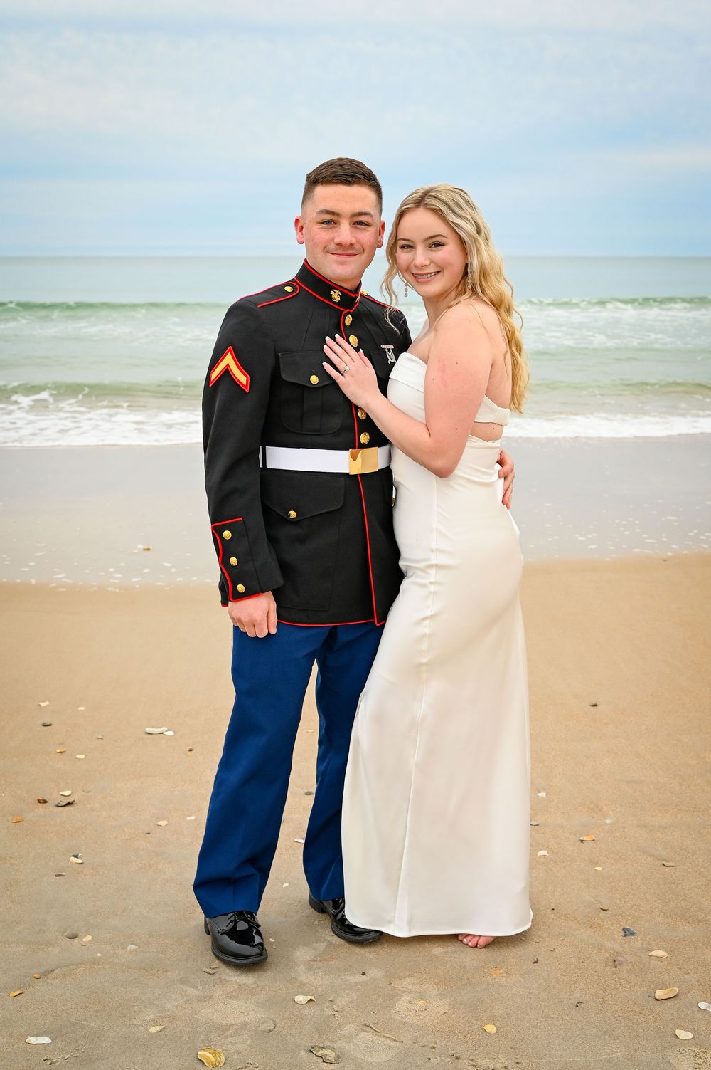 A couple poses for romantic wedding photos on a sandy beach with ocean waves in the background.